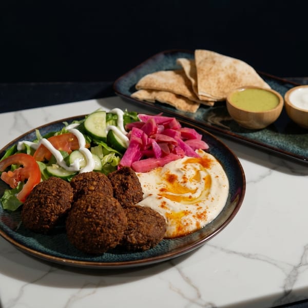 A falafel platter with hummus, salad, pickled turnip, pita bread, and two dipping sauces.