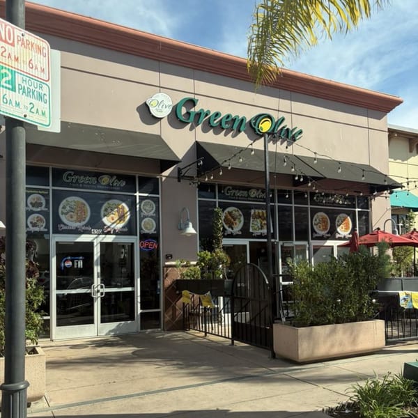 The Green Olive restaurant exterior with a black awning, outdoor seating, and menu displays on the windows.