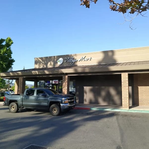 A gray pickup truck parked in front of the Village Mart building on a sunny day.