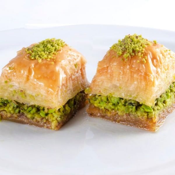 Two pieces of golden baklava, generously filled with bright green pistachios, on a white plate.