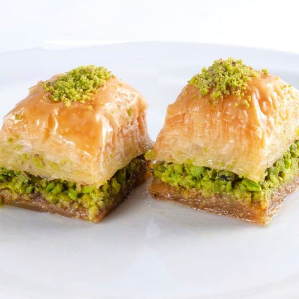 Two pieces of golden baklava, generously filled with bright green pistachios, on a white plate.