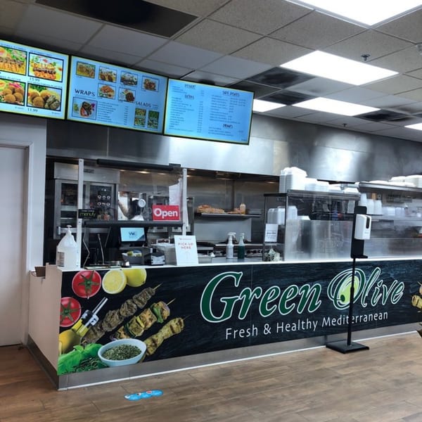The Green Olive restaurant counter with a menu board, food prep area, and brand signage.